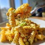 A fork lifts a bite of Vegan Creamy Lemon Chickpea Pasta Salad, showing fusilli pasta coated in a rich, yellow sauce with chickpeas.