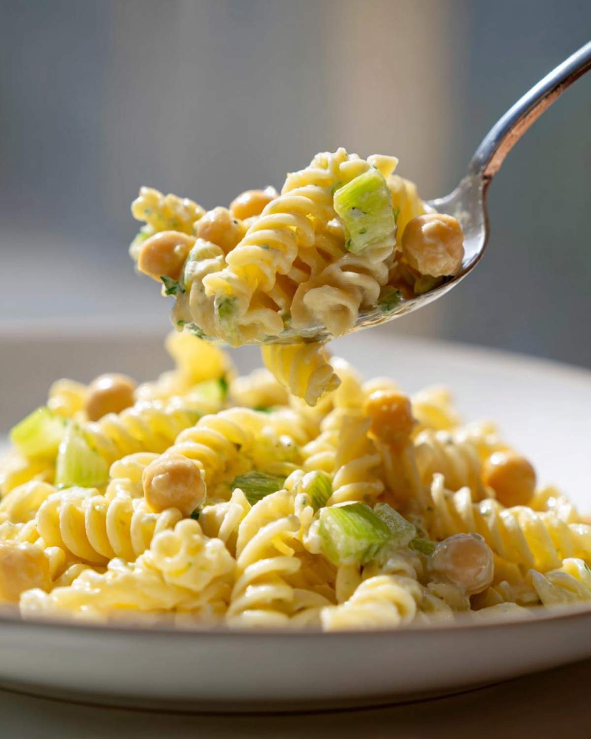 A spoonful of Vegan Creamy Lemon Chickpea Pasta Salad featuring fusilli pasta, chickpeas, and celery in a creamy dressing.