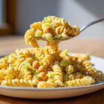 A spoonful of Vegan Creamy Lemon Chickpea Pasta Salad featuring fusilli pasta, chickpeas, and celery, lifted above the main serving plate.