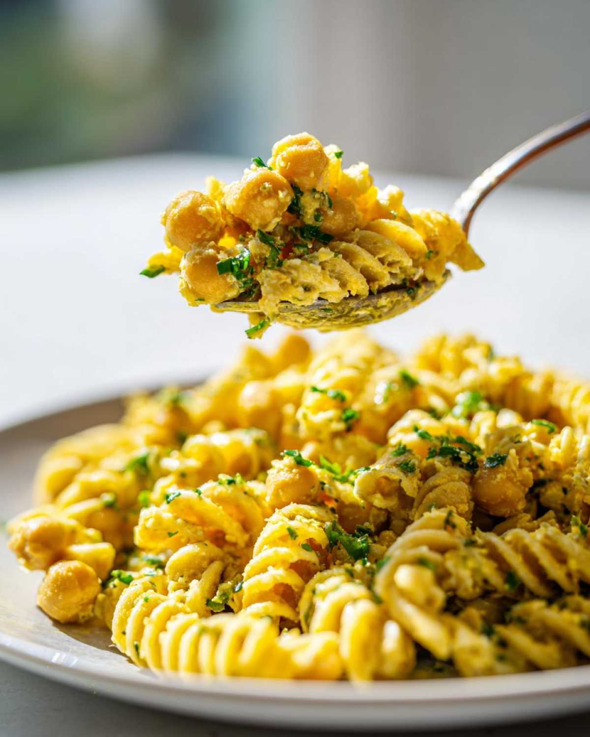 A spoonful of bright yellow Vegan Creamy Lemon Chickpea Pasta Salad being lifted from a plate.
