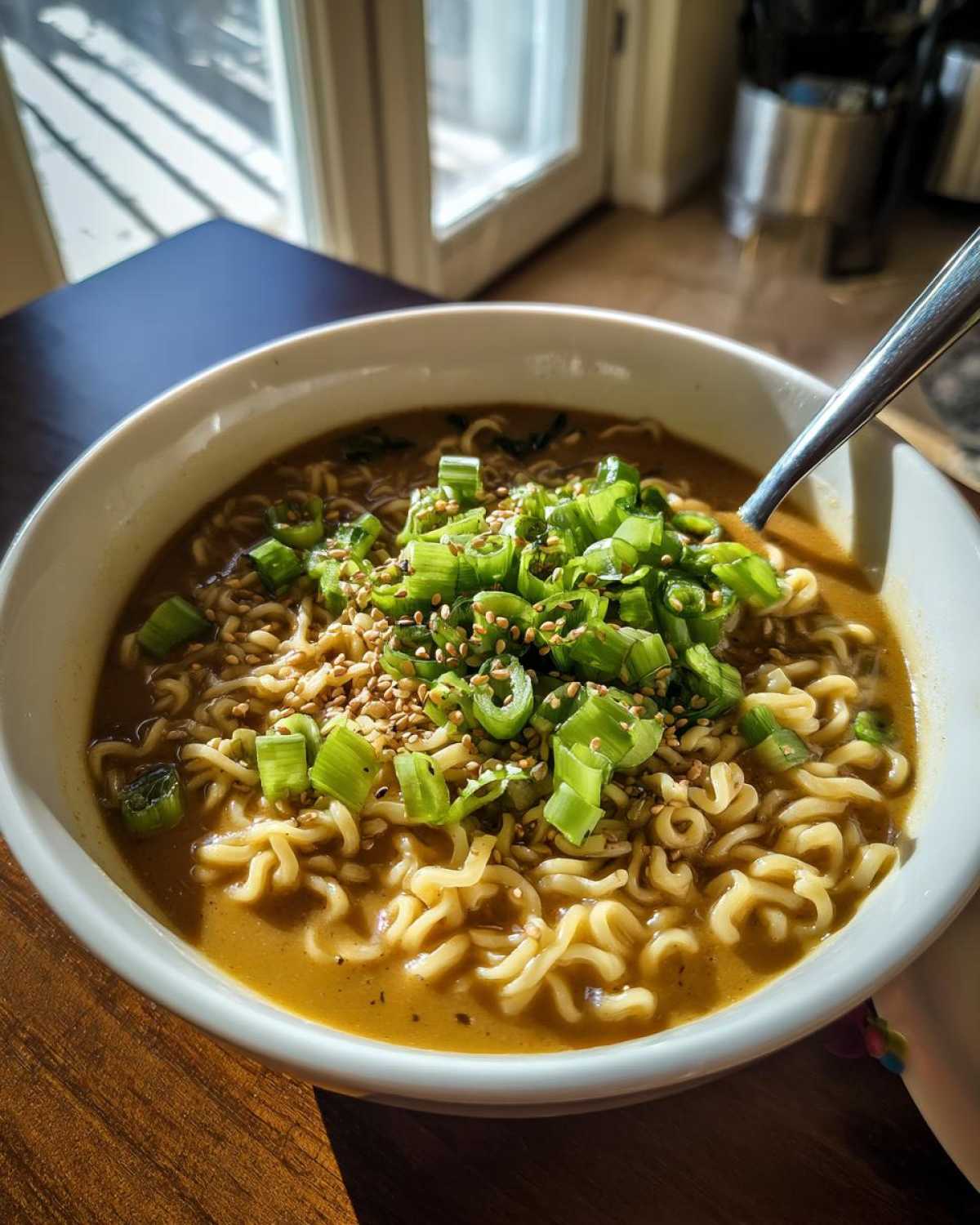 A close-up of a white bowl filled with Vegan Creamy Miso Sesame Noodle Soup, topped generously with chopped green onions and sesame seeds.
