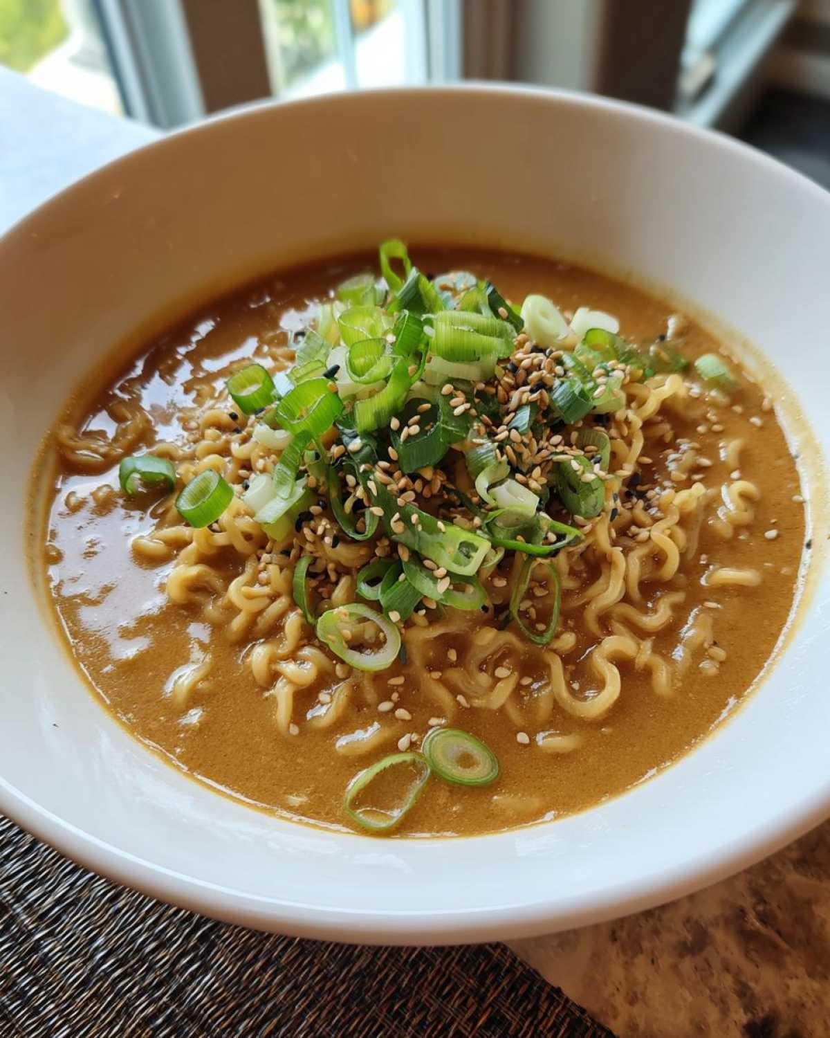 Close-up of a white bowl filled with Vegan Creamy Miso Sesame Noodle Soup, topped with scallions and sesame seeds.