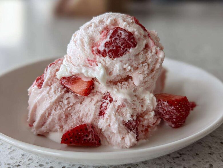 A close-up of scoops of Vegan Creamy Strawberry Oat Milk Ice Cream with visible chunks of fresh strawberries.