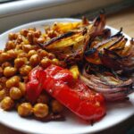 A white plate featuring roasted chickpeas, charred red onion wedges, and a piece of roasted red pepper from the Vegan One-Pan Chickpea Shawarma.