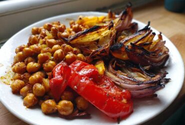 A white plate featuring roasted chickpeas, charred red onion wedges, and a piece of roasted red pepper from the Vegan One-Pan Chickpea Shawarma.