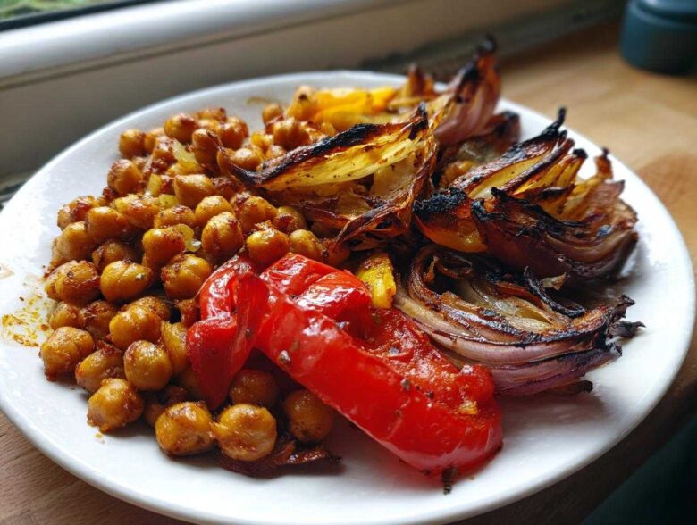 A white plate featuring roasted chickpeas, charred red onion wedges, and a piece of roasted red pepper from the Vegan One-Pan Chickpea Shawarma.