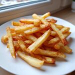 A close-up of a pile of perfectly cooked, golden Air Fryer French Fries served on a white plate.