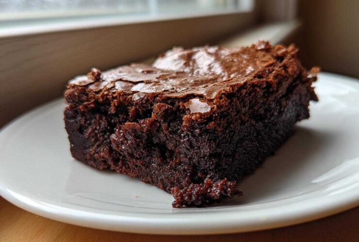 Close-up of a rich, fudgy slice of brownies with a crackly top, sitting on a white plate.