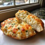 Close-up of an amazing Cheesy Bagel, sliced open to show gooey melted cheese and topped with herbs.