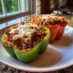 Two halves of Stuffed Bell Peppers, one green and one red, topped with melted cheese, ready to eat.