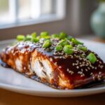 Close-up of a flaky Baked Teriyaki Salmon fillet covered in dark glaze, sesame seeds, and green onions.