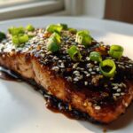 Close-up of a perfectly cooked Baked Teriyaki Salmon fillet covered in dark glaze, sesame seeds, and green onions.