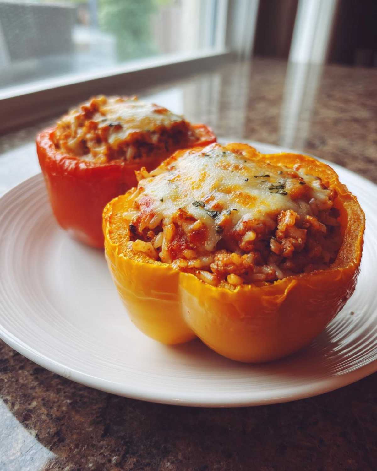 Two colorful Stuffed Bell Peppers, one yellow and one red, topped with melted cheese, served on a white plate.