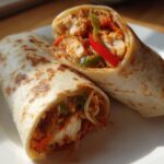Two halves of a delicious Chili Chicken Wraps Lunch, filled with seasoned chicken and colorful peppers, resting on a white plate.
