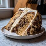 A thick slice of Chocolate Chip Cookie Cake layered with rich frosting, sitting on a small white plate.