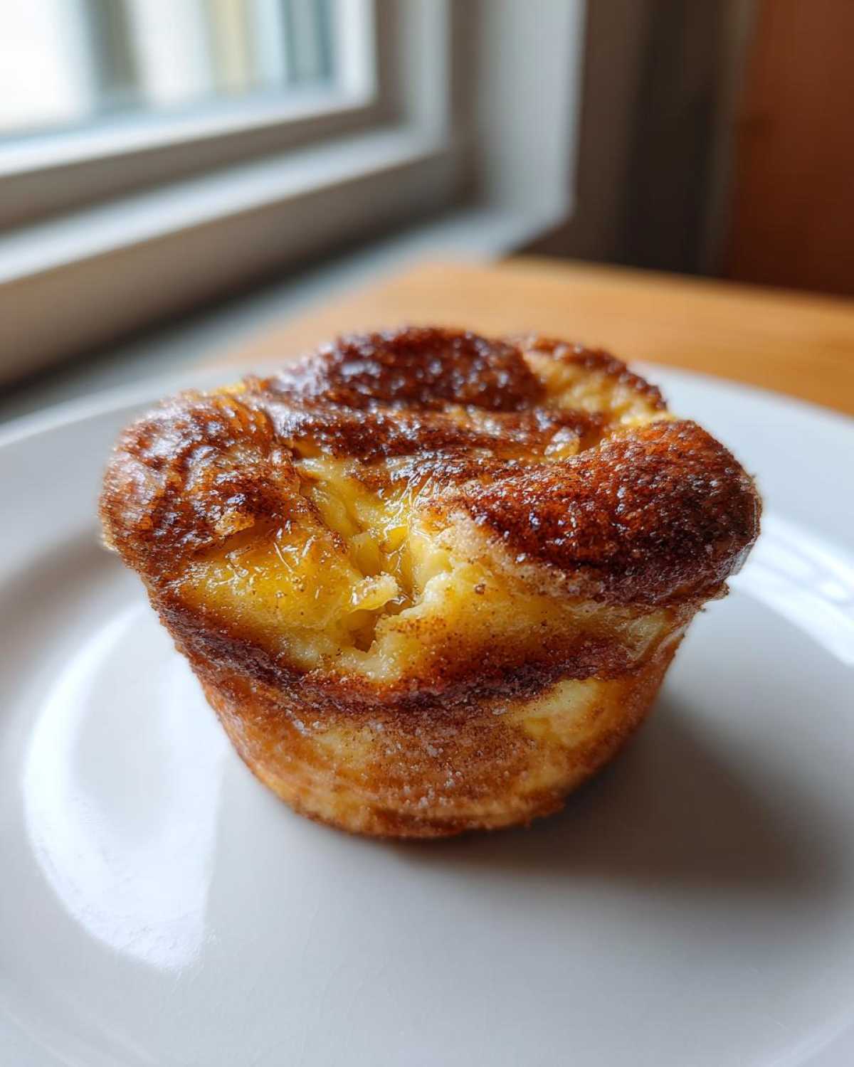A single, golden-brown Cinnamon Sugar French Toast Muffin with a caramelized, sugary top, resting on a white plate.