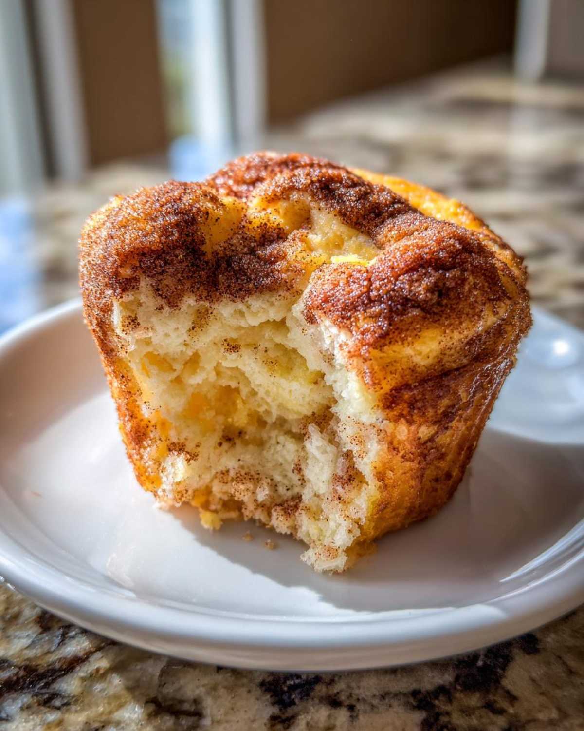 A close-up of a Cinnamon Sugar French Toast Muffins with a bite taken out, showing the fluffy interior and cinnamon topping.
