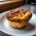 A single, golden Cinnamon Sugar French Toast Muffins with a caramelized, sugary top, resting on a white plate.