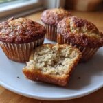 Four golden-brown Cottage Cheese Banana Muffins on a white plate, one cut in half showing the moist interior crumb.