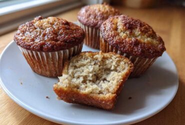 Four golden-brown Cottage Cheese Banana Muffins on a white plate, one cut in half showing the moist interior crumb.