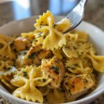 Close-up of Cowboy butter lemon bowtie chicken pasta being lifted by a fork from a white bowl.