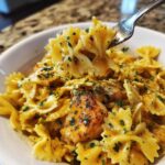 A fork lifts a bite of creamy Cowboy butter lemon bowtie chicken pasta, garnished with parsley.
