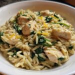 Close-up of creamy chicken orzo with lemon and spinach served in a white bowl.