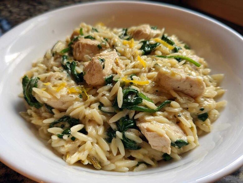 Close-up of creamy chicken orzo with lemon and spinach served in a white bowl.