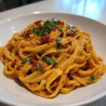 A close-up of creamy Sun-Dried Tomato Pasta tossed with fettuccine, topped with chopped sun-dried tomatoes and fresh basil.