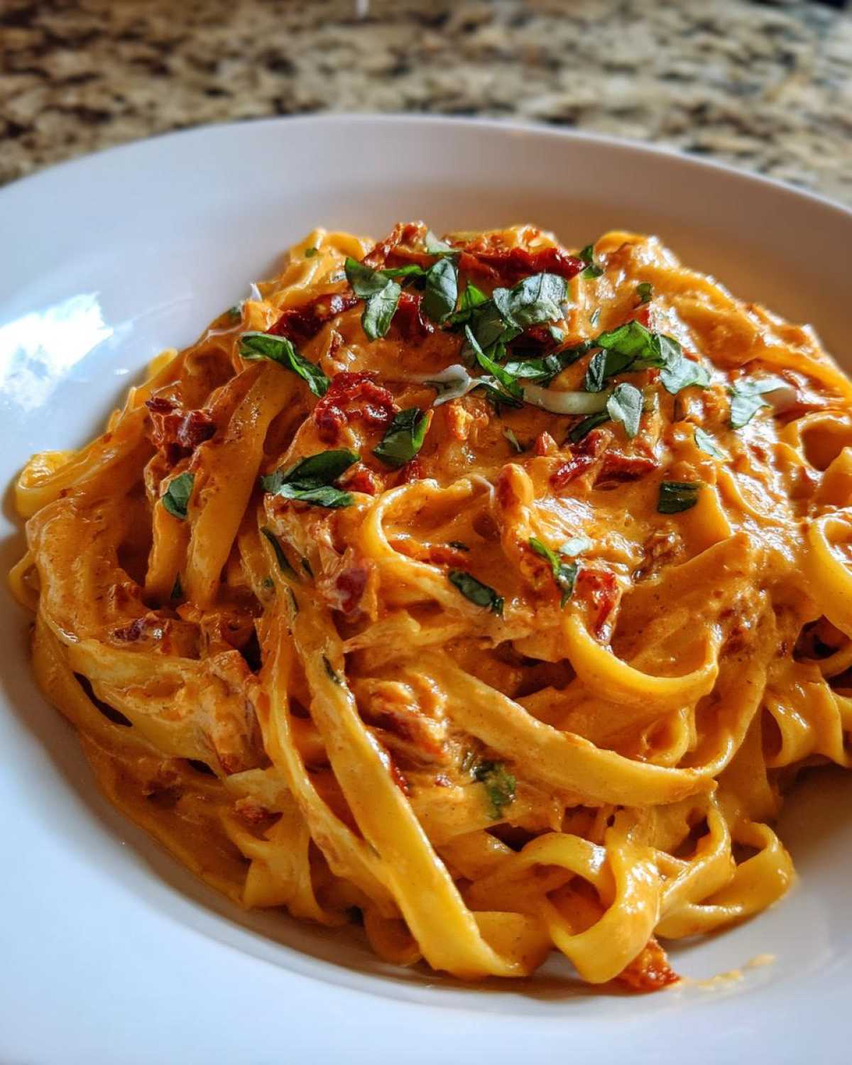 Close-up of creamy fettuccine Sun-Dried Tomato Pasta topped with fresh basil.