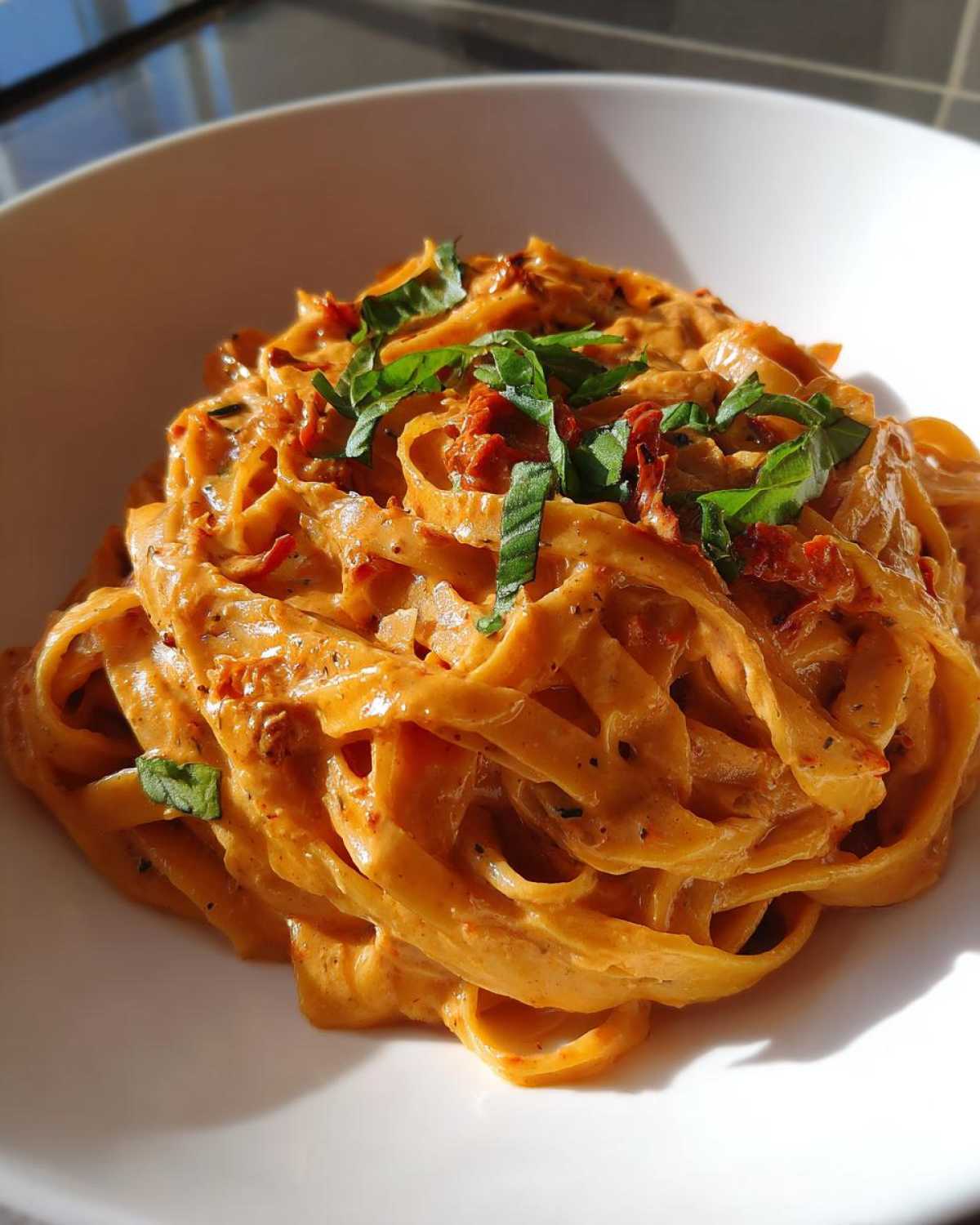 Close-up of creamy Sun-Dried Tomato Pasta tossed with fettuccine and topped with fresh basil.