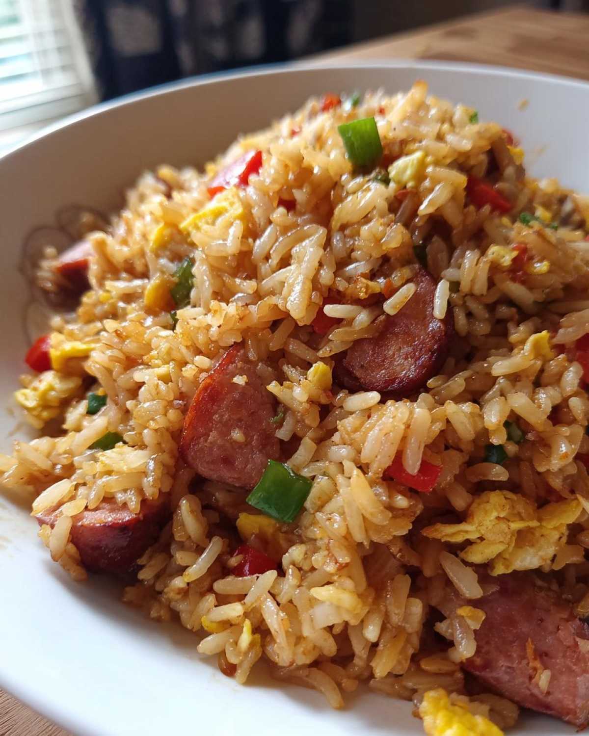 Close-up of a bowl filled with flavorful Creole Garlic Fried Rice featuring sausage slices, scrambled egg, and colorful peppers.