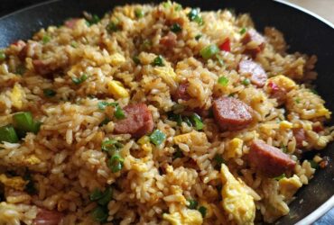 A close-up view of savory Creole Garlic Fried Rice featuring sausage slices, scrambled egg, and green onions in a dark skillet.