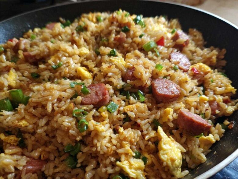 A close-up view of savory Creole Garlic Fried Rice featuring sausage slices, scrambled egg, and green onions in a dark skillet.