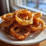 Golden brown, crispy onion rings piled on a white plate, made using the Air Fryer Onion Boil method.