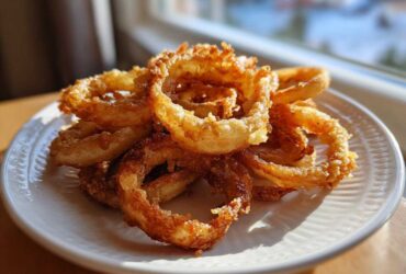 Golden brown, crispy onion rings piled on a white plate, made using the Air Fryer Onion Boil method.