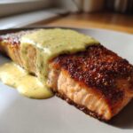 Perfectly cooked Crispy Pan Seared Salmon topped with creamy lemon dill sauce on a light plate.