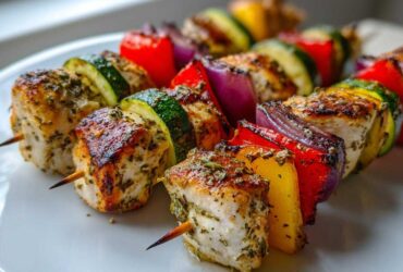 Close-up of grilled Easy Chicken Skewer Recipe for Summer Dinner featuring seasoned chicken, zucchini, red onion, and bell peppers on a white plate.