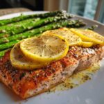A perfectly cooked fillet of Garlic Butter Baked Salmon Dinner topped with lemon slices and served with roasted asparagus.