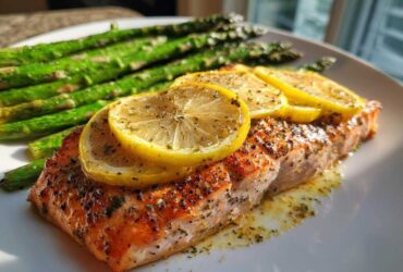 A perfectly cooked fillet of Garlic Butter Baked Salmon Dinner topped with lemon slices and served with roasted asparagus.