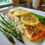 Close-up of a perfectly cooked Garlic Butter Baked Salmon Dinner topped with lemon slices and served alongside roasted asparagus.