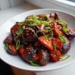 A close-up of savory Gochujang Mushrooms coated in a rich red sauce, garnished with green onions and sesame seeds.