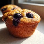 Close-up of a perfectly baked, golden-brown Blueberry Muffins top featuring burst, juicy blueberries.
