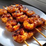 Close-up of succulent Grilled Honey Garlic Shrimp skewers coated in a glossy, caramelized sauce and sesame seeds on a white plate.