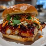 Close-up of a juicy Korean BBQ Chicken Sandwich featuring thick, glazed chicken, slaw, and cilantro on a soft bun.