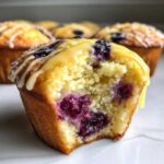 Close-up of a Lemon Blueberry Muffins with a bite taken out, showing moist interior and lemon glaze dripping.