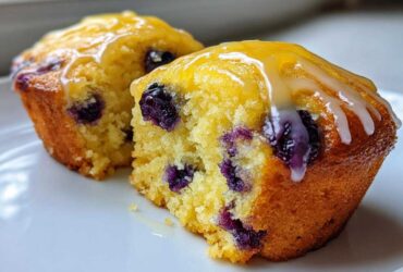 Cross-section of two Lemon Blueberry Muffins topped with a bright yellow lemon glaze.