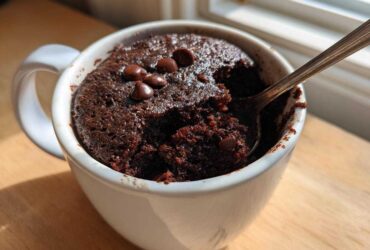 Close-up of a rich, dark Microwave Brownie in a Mug, topped with chocolate chips and being eaten with a spoon.