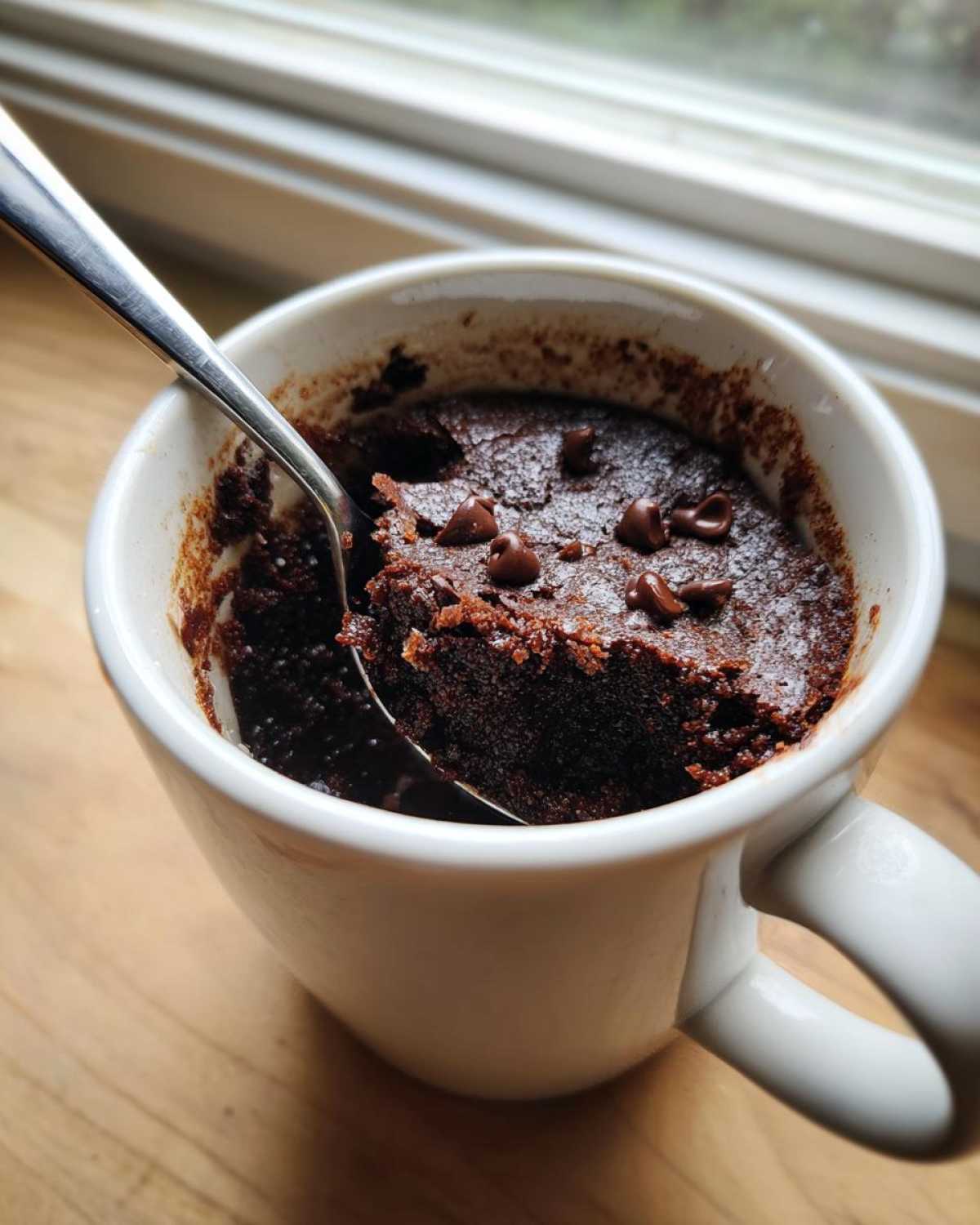 A rich, dark chocolate Microwave Brownie in a Mug being scooped with a silver spoon, topped with chocolate chips.