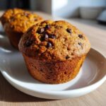 Close-up of a perfectly baked Banana Chocolate Chip Muffins, golden brown with melted chocolate chips on top.